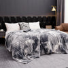 A gray and white tie-dye flannel fleece throw blanket draped over a bed in a modern bedroom setting.