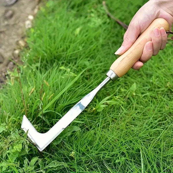 A hand holds a stainless steel L-shaped weeding tool with a wooden handle, positioned on green grass.