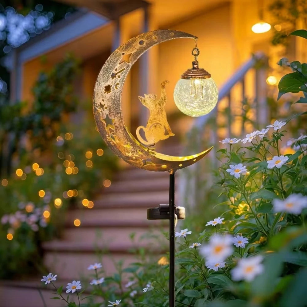 A solar owl garden light with moon decor hangs over a staircase surrounded by flowering plants.