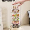 A hand rotates a transparent display case filled with various small collectible figures for 360 degree appreciation.