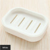 A white compact travel soap holder with a secure lid is shown on a light wooden surface.