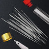 A set of stainless steel sewing needles and a travel case are displayed on a dark surface.