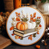 Cross stitch kit featuring a fall pumpkin design on a white fabric with embroidery tools.