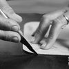 Nahaufnahme, eine Hand benutzt ein Messer, um Leder zu schneiden, von einem Handwerker namens S.WORKER Leather Artist.