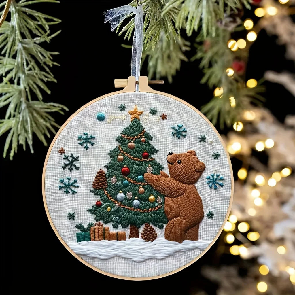 A circular embroidery hoop featuring a handcrafted Christmas tree with ornaments and a teddy bear, set against a dark backgro