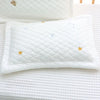A white quilted baby pillow with gold stars and blue crescent moons resting on a white textured fabric.