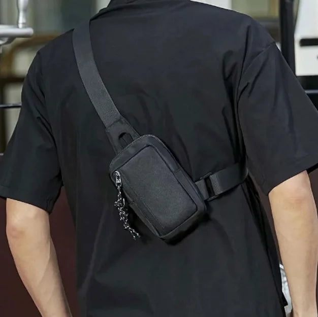 A person wearing a black t-shirt is shown from the back, carrying a black canvas crossbody bag on their shoulder.