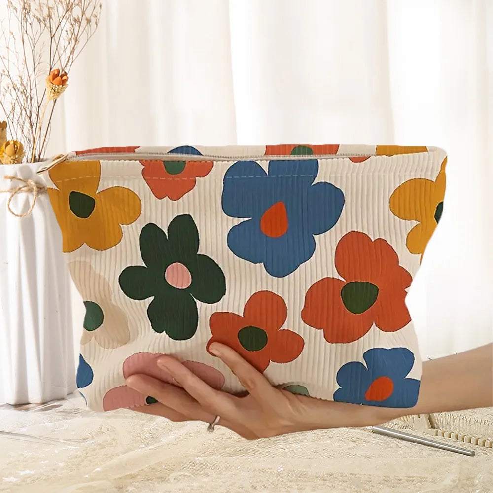 A hand holds a floral corduroy makeup bag with a secure zipper, featuring orange, yellow, and blue flowers.