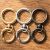 A collection of round spring snap hooks in gold and silver metal alloys arranged on a wooden surface.