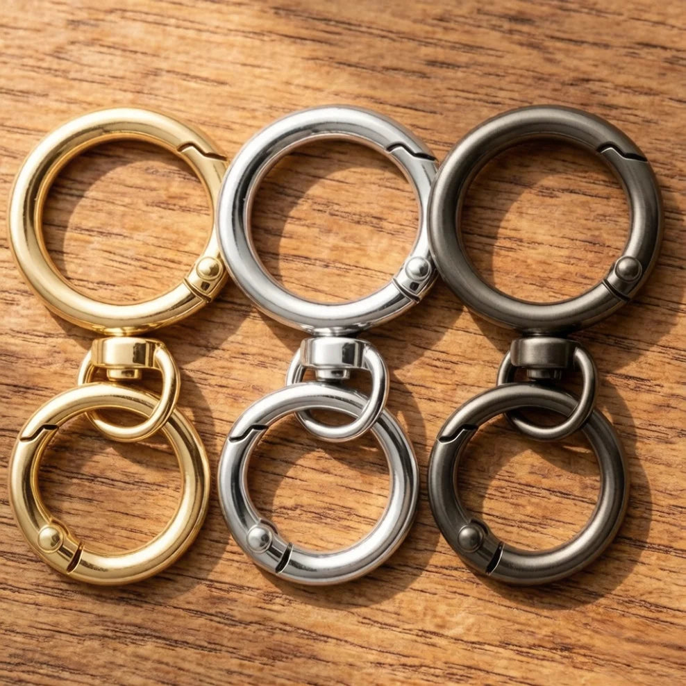 A collection of round spring snap hooks in gold and silver metal alloys arranged on a wooden surface.