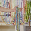 A hand is holding a long, colorful tassel string curtain made of multicolored threads.