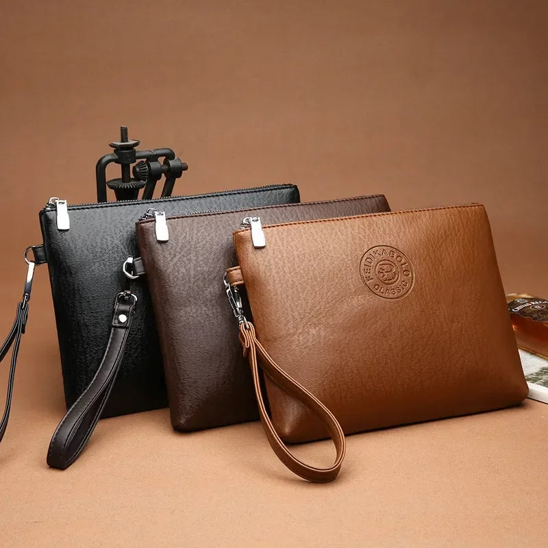 Braunes Lederclutch-Portemonnaie mit Messinglogo und schwarzem Lederriemen auf neutralem Hintergrund