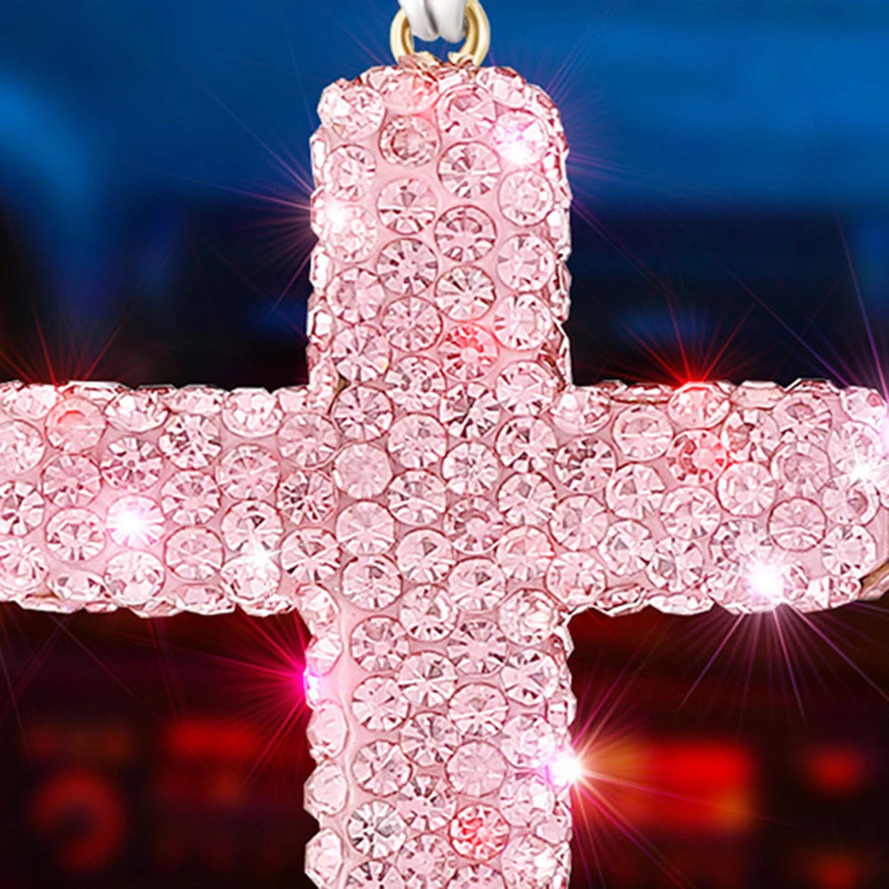 Pink rhinestone cross pendant hanging from a white loop.