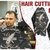A black waterproof hair cutting cape with a barber theme is shown in a professional salon setting.