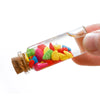 A hand holds a clear glass bottle filled with colorful glass beads and a cork stopper for DIY crafts.