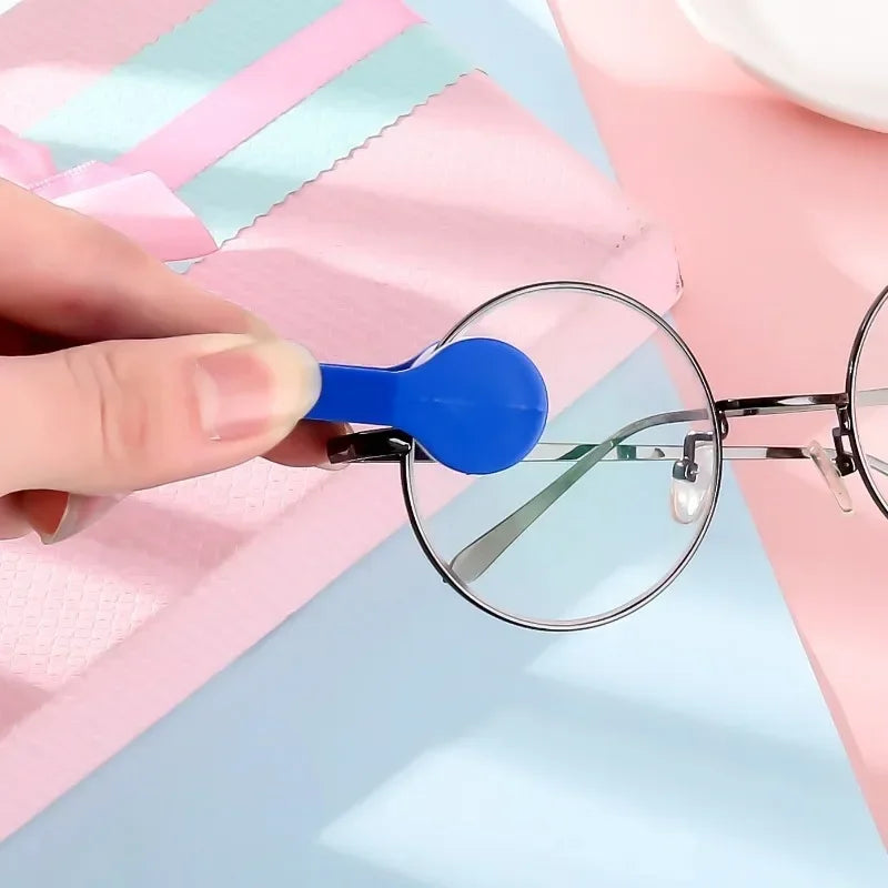 A hand holds a blue cleaning brush attached to a pair of eyeglasses on a pink background.