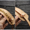 A close-up of a tan genuine leather handbag handle wrap and shoulder pad being held by a hand.