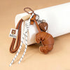 A braided leather croissant keychain with a brown bag pendant and white cord on a light background.