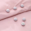 Six round white non-slip clips are arranged on a soft pink fabric surface.