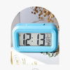 A light blue compact LED digital clock displaying 12:13, featuring a temperature display and alarm functions.