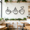 A set of three black iron art coffee cup wall decor pieces displayed on a white wall above wooden tables.
