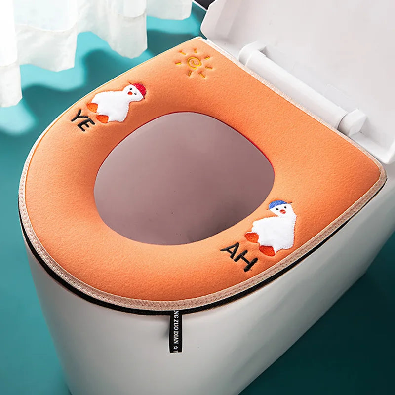 Tapa impermeable naranja para inodoro de peluche con figuras decorativas pequeñas en la tapa.