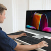A man is using an extended anti-slip desk pad with stitched edges on a laptop.