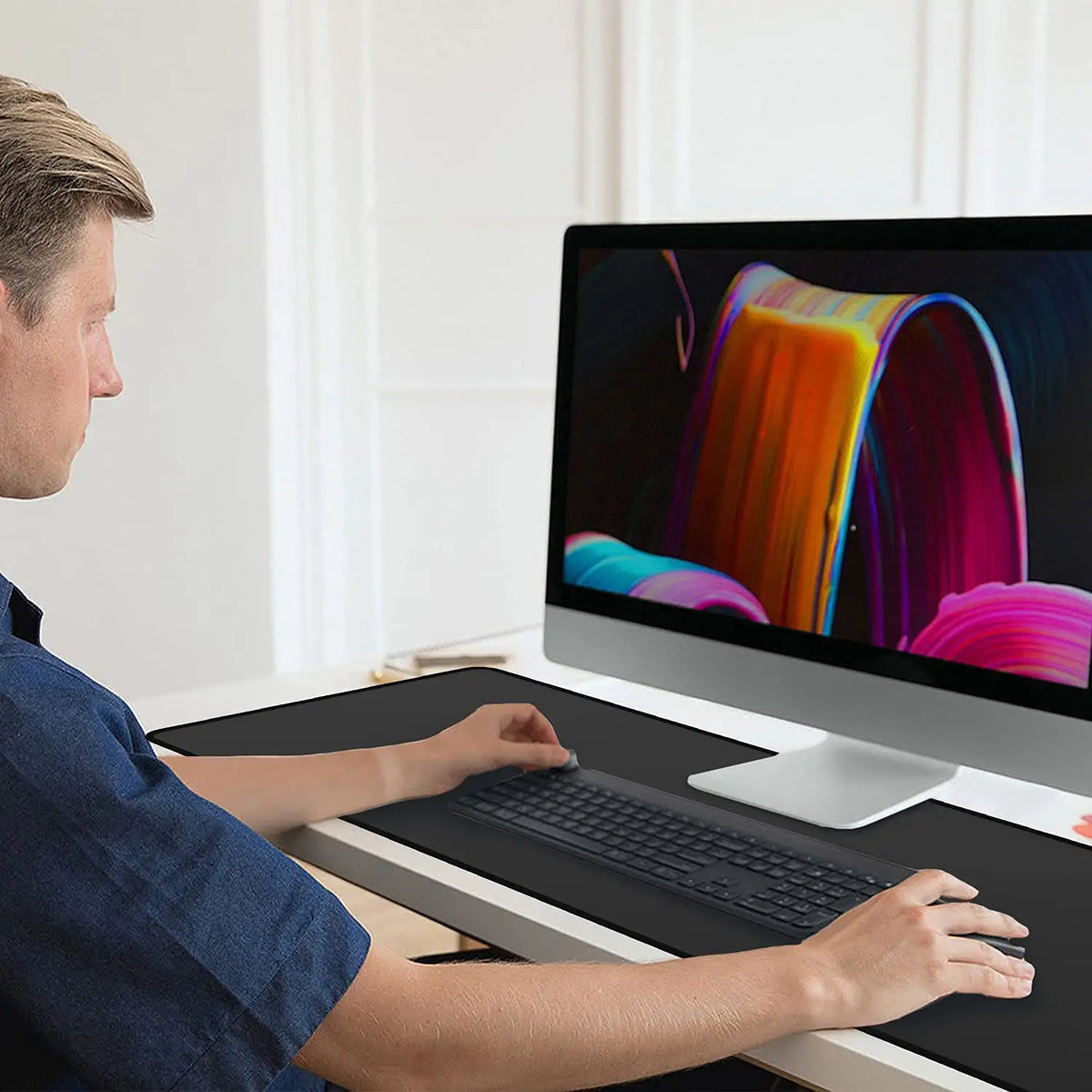 A man is using an extended anti-slip desk pad with stitched edges on a laptop.