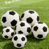 A pile of realistic black and white football plush toys resting on green grass.