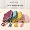 A collection of tassel jewelry bags in purple, blue-green, olive green, and pink velvet are displayed on a light surface.