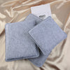 A pair of gray felt mats for wool crafting resting on a satin fabric with a card.