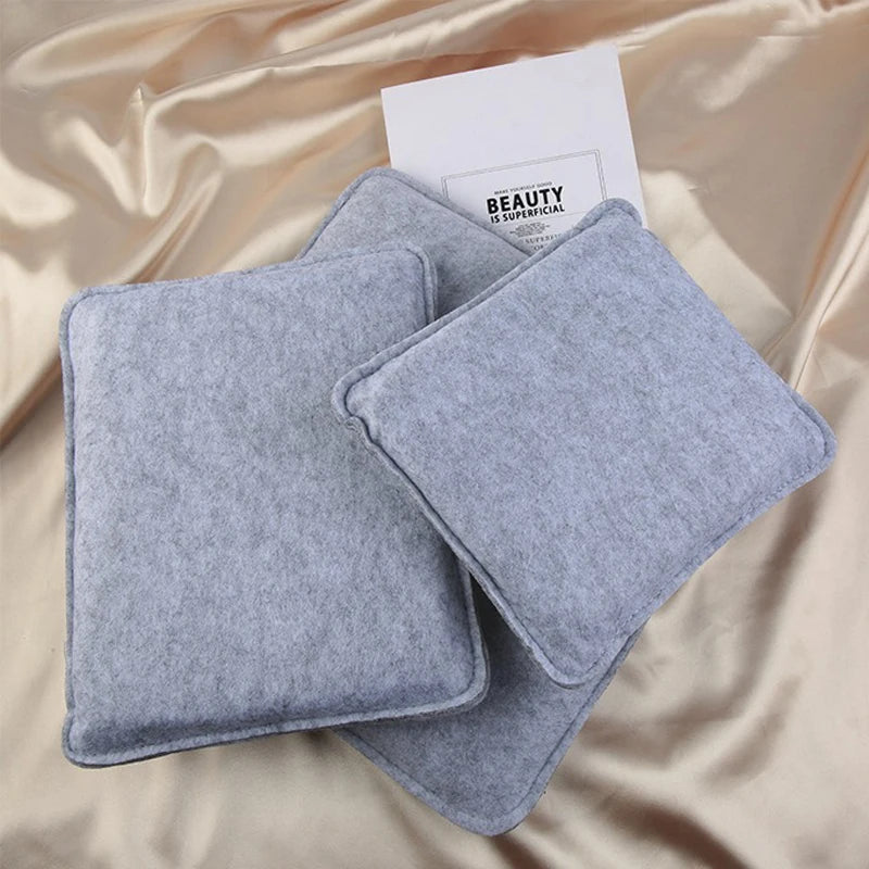 A pair of gray felt mats for wool crafting resting on a satin fabric with a card.