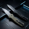 A folding pocket knife with a gray blade and a tan handle resting on a dark surface.