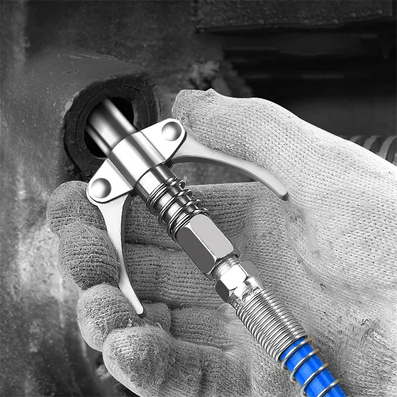 A hand holds a heavy-duty grease gun coupler with a silver metal body and blue tip.