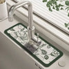 A modern chrome faucet mounted on a dark green floral patterned mat in a kitchen sink.