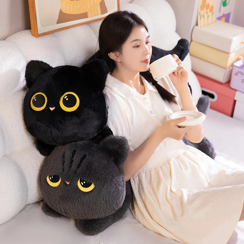 A woman is relaxing and drinking tea while cuddling a soft black cat plush toy on a white sofa.