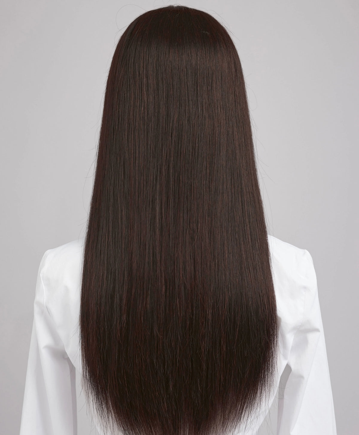 Una peluca de cabello humano largo, liso y marrón oscuro de seda, mostrada desde atrás sobre un fondo gris claro.