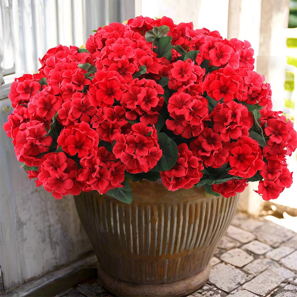 A vibrant bouquet of red artificial geranium flowers in a terracotta pot