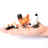 A hand holds several realistic animal figurines, including a rooster and a chicken, for a farm and wildlife collection.