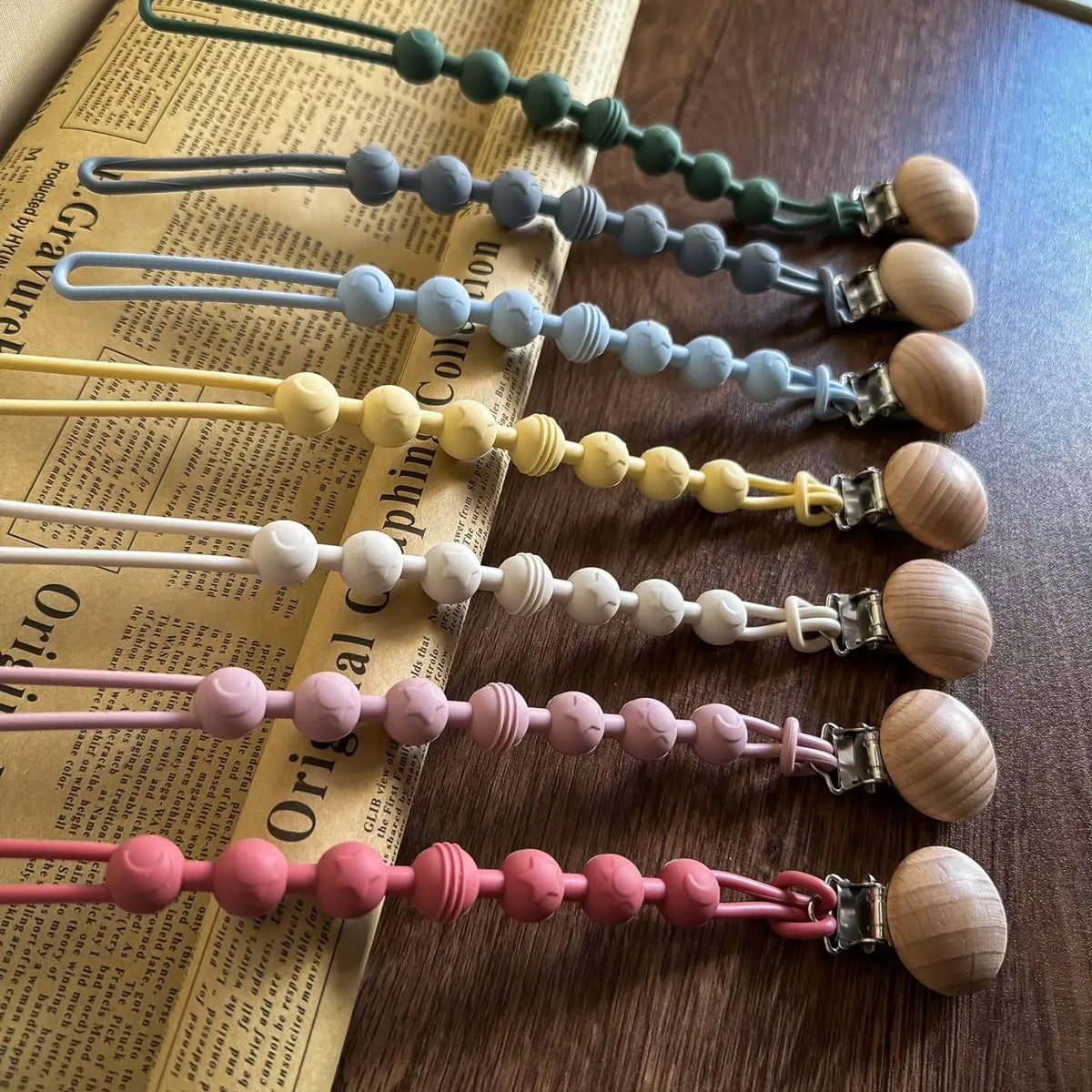 A collection of silicone pacifier clips and teethers in various shades of green, blue, yellow, and pink arranged horizontally