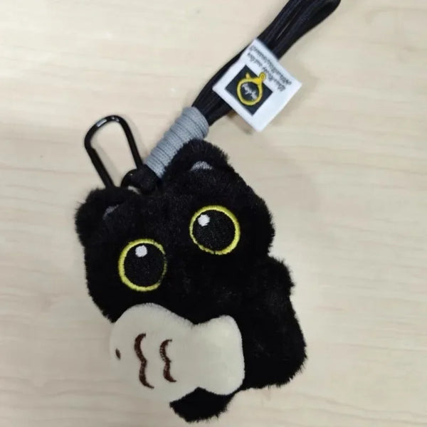 Clé-poussette de chat en peluche noire avec des yeux jaunes et une patte blanche, attachée à un cordon noir.