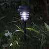 A black solar-powered mosquito zapper with an ambient light illuminates the surrounding grass.