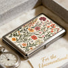 A vintage metal card and cash case with an Art Deco floral design resting on a light fabric.