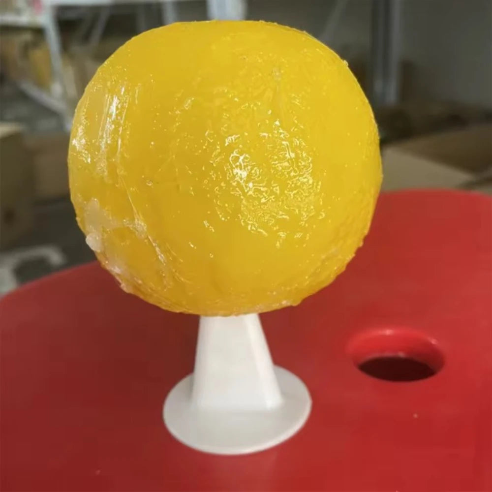 A bright yellow sticky fruit fly trap ball on a white stand for pest control.