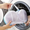A hand is placing a white mesh laundry bag for bras and lingerie into the drum of a washing machine.