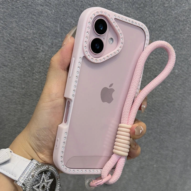 Una mano sostiene una funda rosa para iPhone con diseño transparente de diamante y una correa de muñeca rosa.