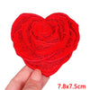 A bright red heart-shaped embroidery patch with a rose design being held by a hand.