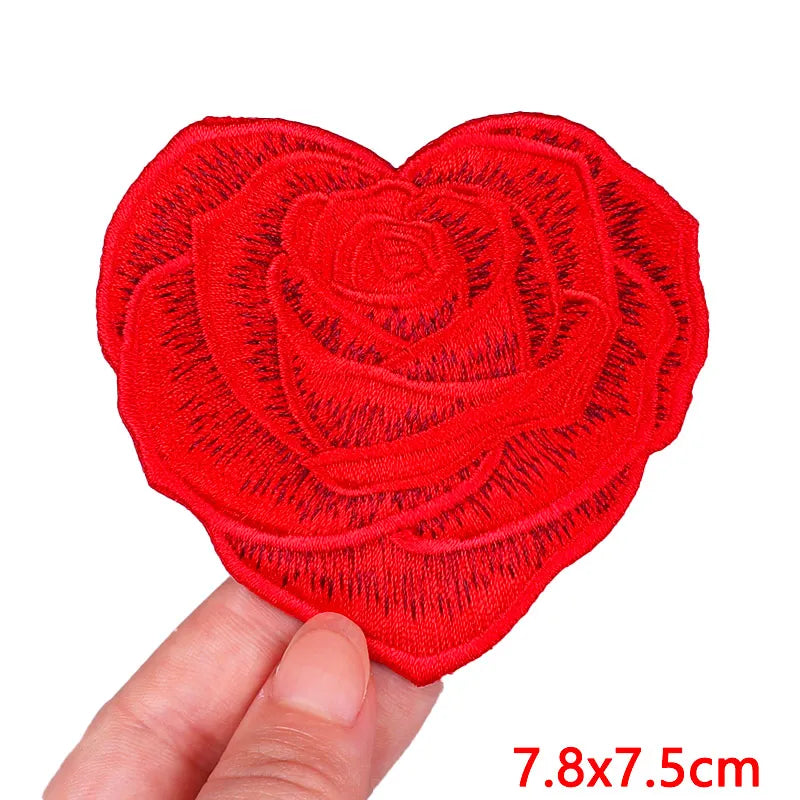 A bright red heart-shaped embroidery patch with a rose design being held by a hand.