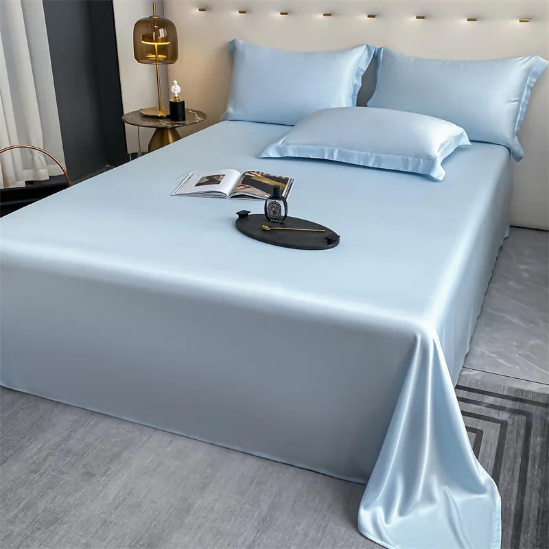 A light blue luxury bamboo flat sheet is neatly folded on a bed with matching pillows and a book.