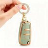 A hand holds a protective TPU key fob cover for Audi flip keys with a gold-tone ring and fob.